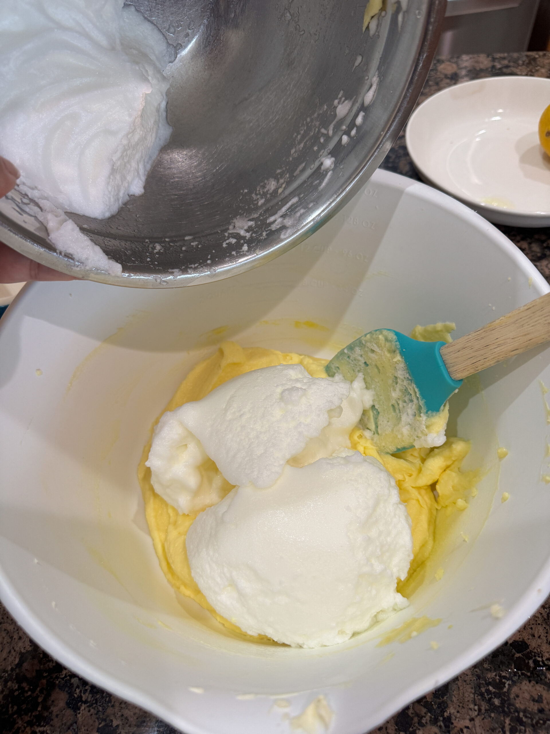 stiff egg whites being added to egg yolks and sugar in a bowl